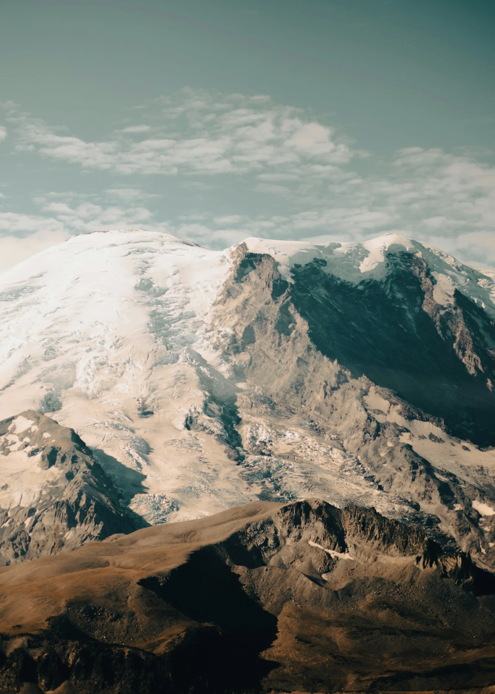 A snow-covered mountain range beneath an open, cloud-dappled sky.